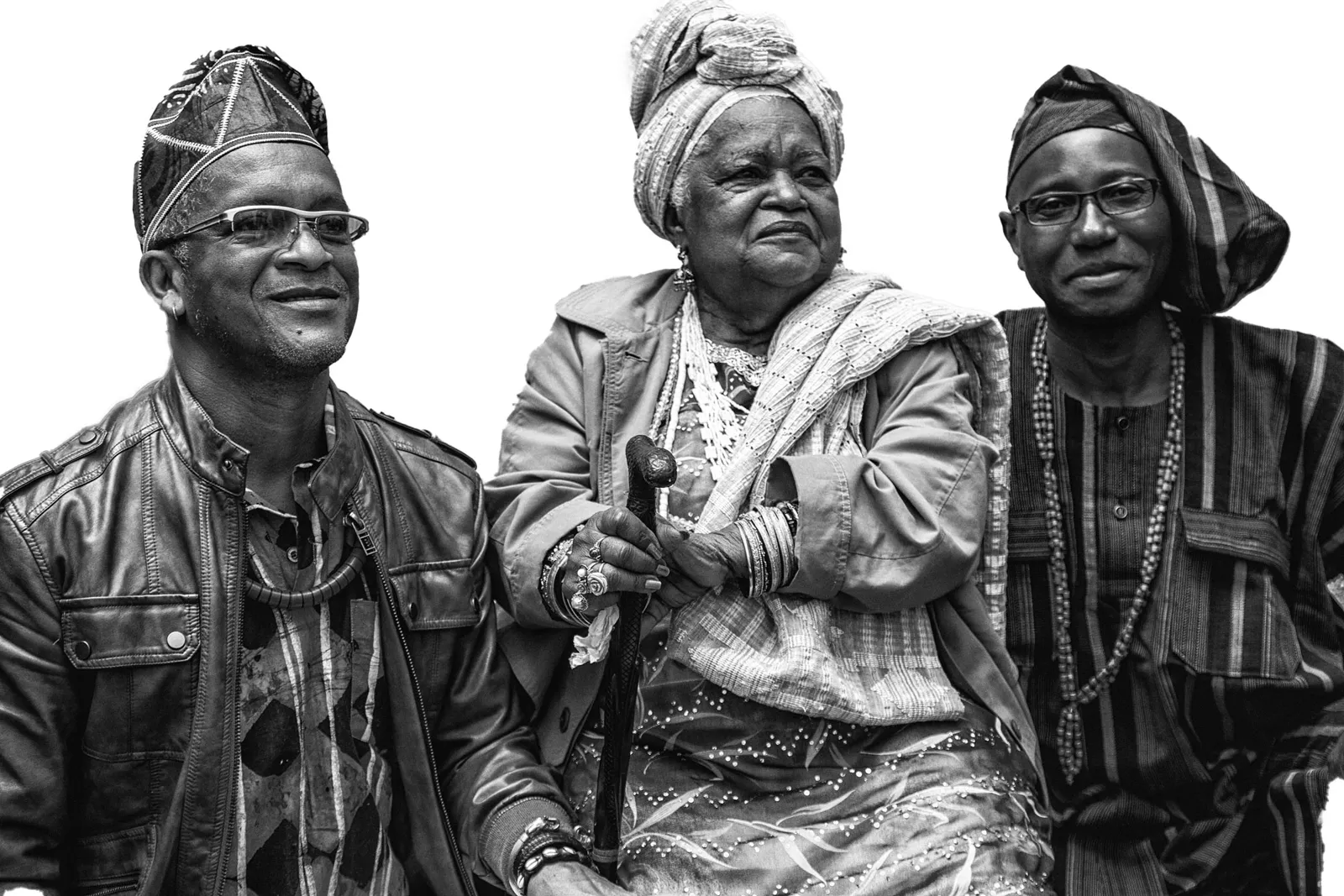 Three people in Yorùbá dress, an elder seated between two men